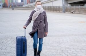 γυναίκα με βαλίτσα στο αεροδόμιο φοράει μάσκα προστασία για μετάλλαξη ιού covid19