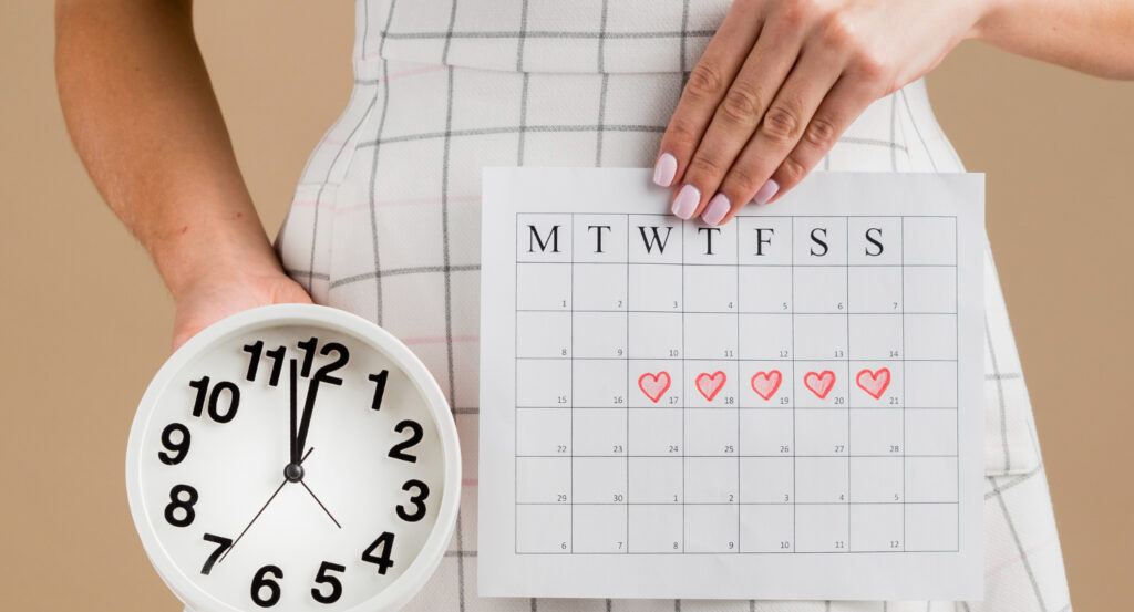 γυναίκα κρατάει ρολόι και ημερολόγιο υπολογιμού εβδομάδων εγκυμοσύνης